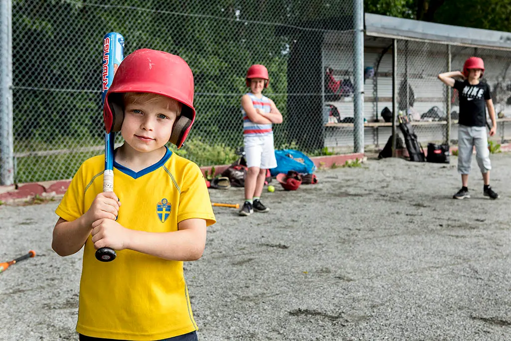 Liten pojke som håller i ett basebollracket på en baseballarena.