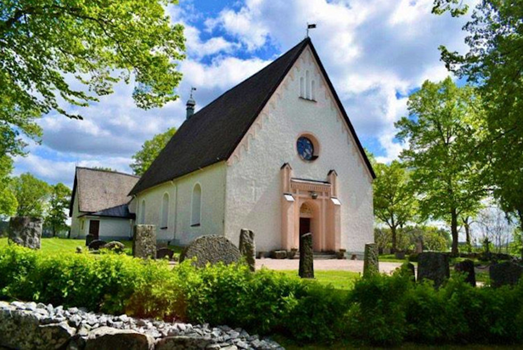 Bild på Löt kyrka. En vit stenbyggnad med orangeaktiga detaljer runt dörren och vid takets kant.