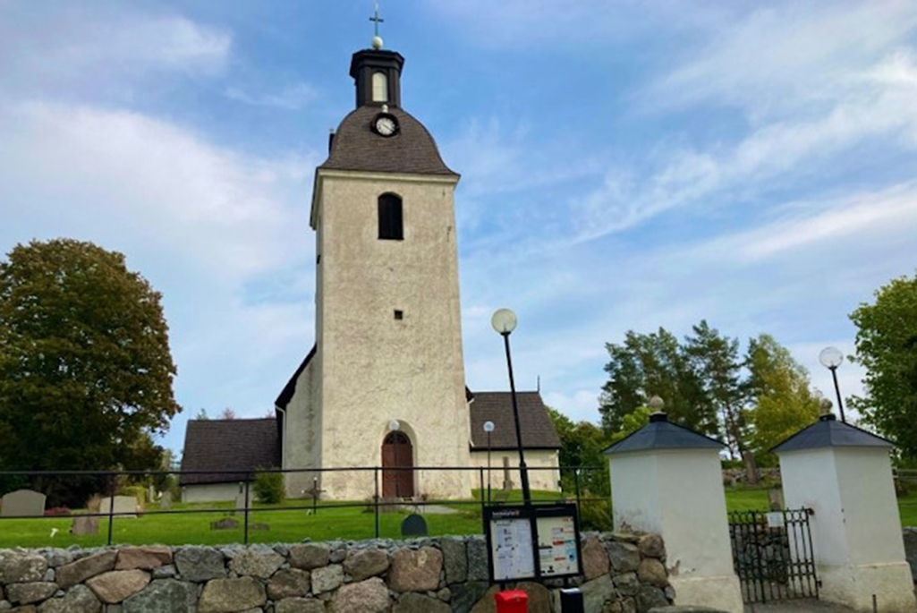 Bild på Husby-sjutolft kyrka. En gulaktig stenbyggnad med ett högt torn.