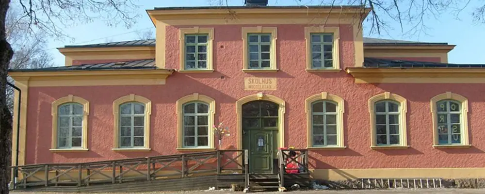 Foto av Säfsta ekologiska förskola. Det är en rödaktig flervåningsbyggnad med gula knutar. 