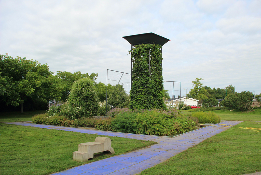 Foto på Blå trädgård. Hela parken syns i bilden. I förgrunden går den blå gången till parken. I parken ser man det höga humletornet, och lummiga växter.