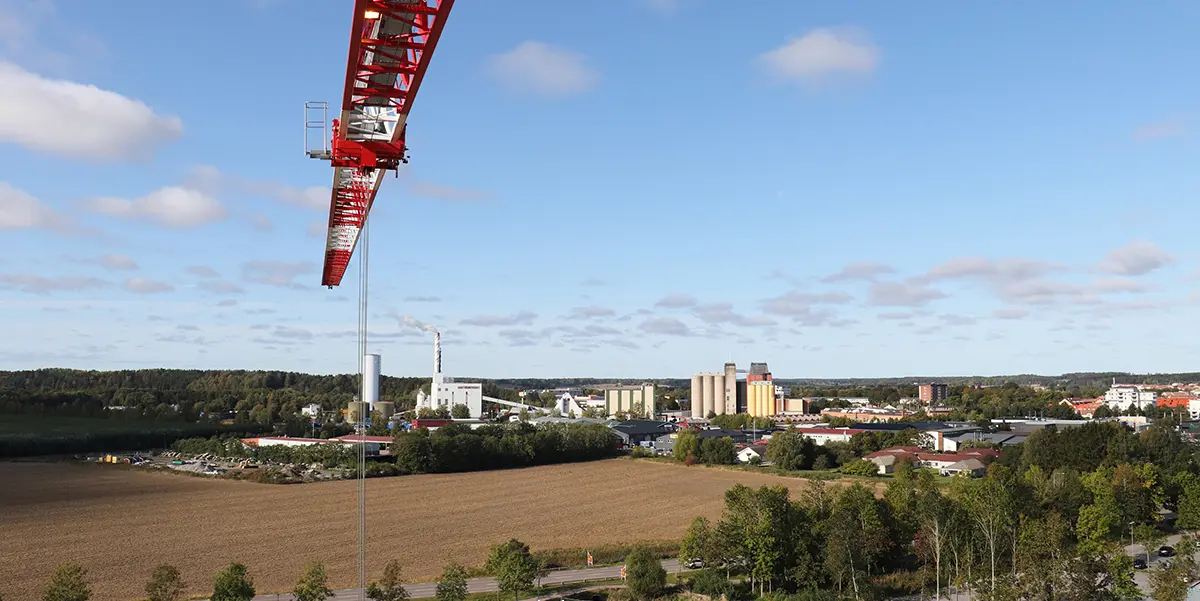 Foto taget från en lyftkran. I bildens topp syns lyftkranens kran i rött och vitt. I bakgrunden syns en del av Enköpings stad. 